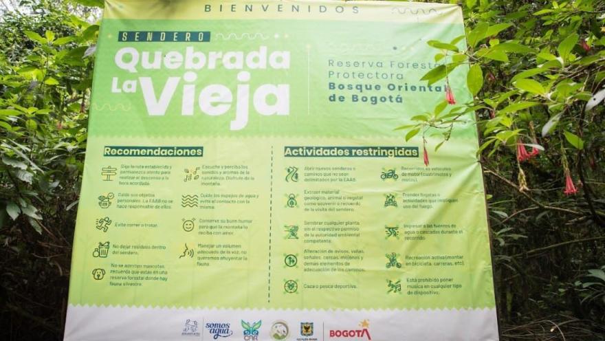 An information sign for the Quebrada La Vieja trail, located in the Eastern Forest Reserve of Bogotá. The sign, surrounded by vegetation, presents recommendations for visitors and conservation rules to protect this natural environment.