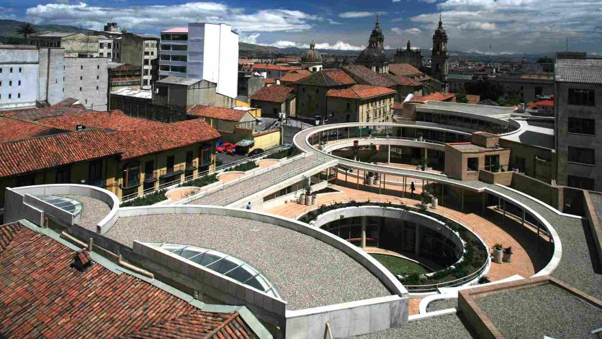 Vista panorámica del Centro Cultural Gabriel García Márquez en el centro histórico de Bogotá. Destacan sus terrazas y corredores curvos de concreto y ladrillo, diseñados por Rogelio Salmona, integrados con los tejados coloniales de La Candelaria y las cúpulas de iglesias históricas bajo un cielo azul con nubes.