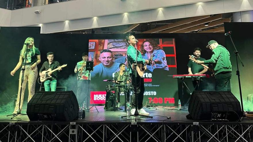Banda musical se presenta en tarima dentro del centro comercial Nuestro Bogotá durante un evento en vivo con pantallas y luces.