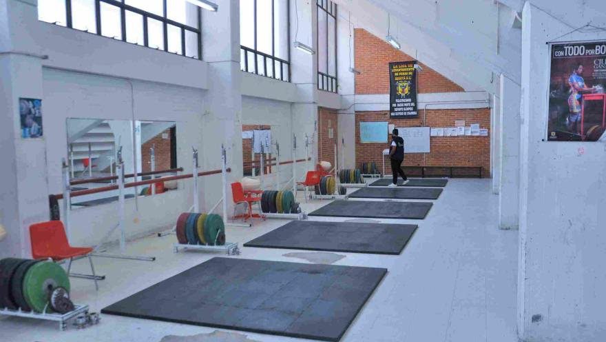 Sala de levantamiento de pesas del Coliseo Cayetano Cañizares, equipada con plataformas de entrenamiento, barras olímpicas y discos de diferentes pesos, en un espacio especializado para la preparación y el desarrollo de atletas de alto rendimiento.