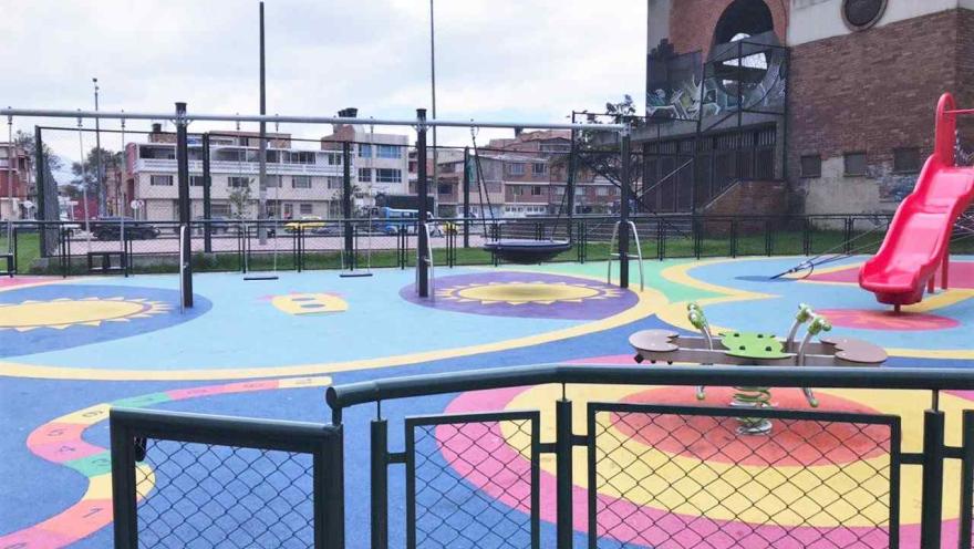 Zona de juegos infantiles al aire libre junto al Coliseo Cayetano Cañizares, equipada con columpios, resbaladero y juegos interactivos sobre una superficie colorida y segura, diseñada para la recreación y el disfrute de niños y familias.