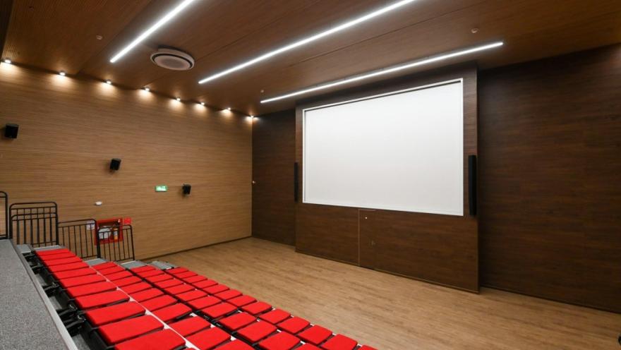Auditorio del Centro Felicidad Cometas con graderías de sillas rojas, pantalla de proyección de gran formato y diseño moderno, un espacio destinado a actividades culturales, académicas y comunitarias.