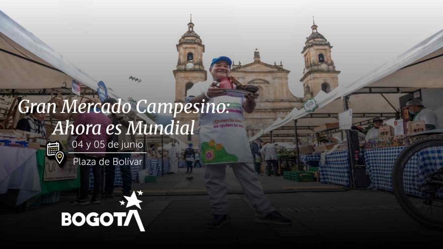 Un hombre posa en la Plaza de Bolívar sosteniendo productos agrícolas, con la Catedral Primada al fondo en un día claro.