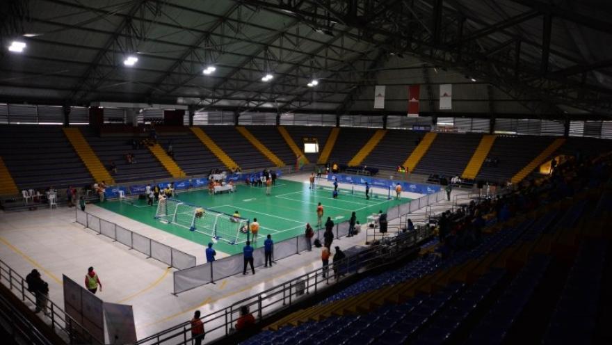 Vista interior del Palacio de los Deportes de Bogotá durante un torneo de bádminton, con varias canchas en competencia y graderías que rodean el escenario deportivo.