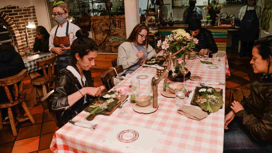 Personas participan en una experiencia gastronómica alrededor de una mesa, mientras disfrutan platos servidos en un ambiente cálido y acogedor de restaurante.