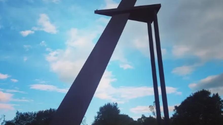 Escultura monumental de acero ubicada en el Centro de Alto Rendimiento de Bogotá, rodeada de zonas verdes y enmarcada por un cielo parcialmente nublado.