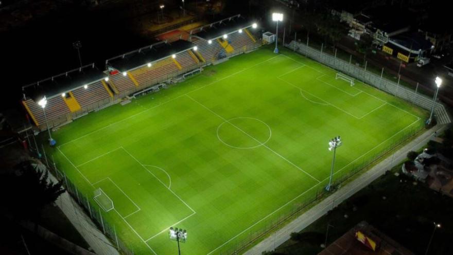  Vista aérea nocturna del Estadio Olaya Herrera con la cancha de fútbol iluminada, graderías a un costado y reflectores encendidos alrededor del escenario deportivo.