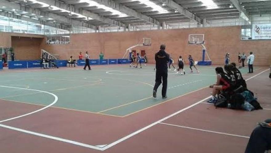 Vista interior de un coliseo del Centro de Alto Rendimiento de Bogotá durante un partido de baloncesto, con jugadores en competencia y espectadores en las graderías laterales.