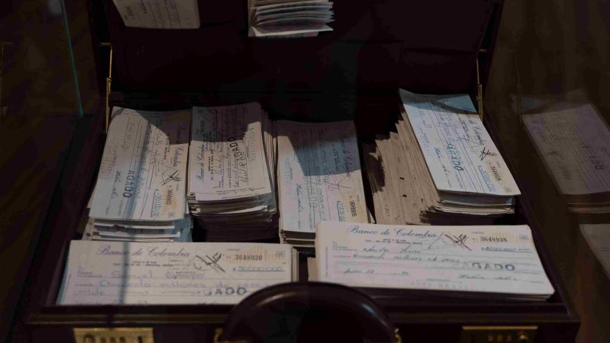 Maletín abierto con numerosos cheques antiguos del Banco de Colombia, exhibidos como documentos históricos en un espacio museístico.