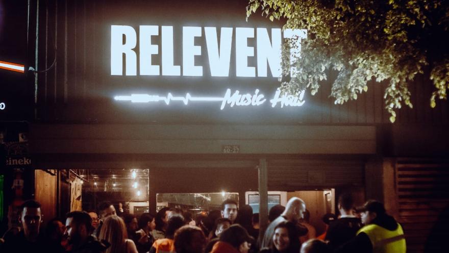  Fachada iluminada de Relevent Music Hall durante la noche, con un grupo de personas reunidas en la entrada bajo el letrero luminoso del establecimiento.