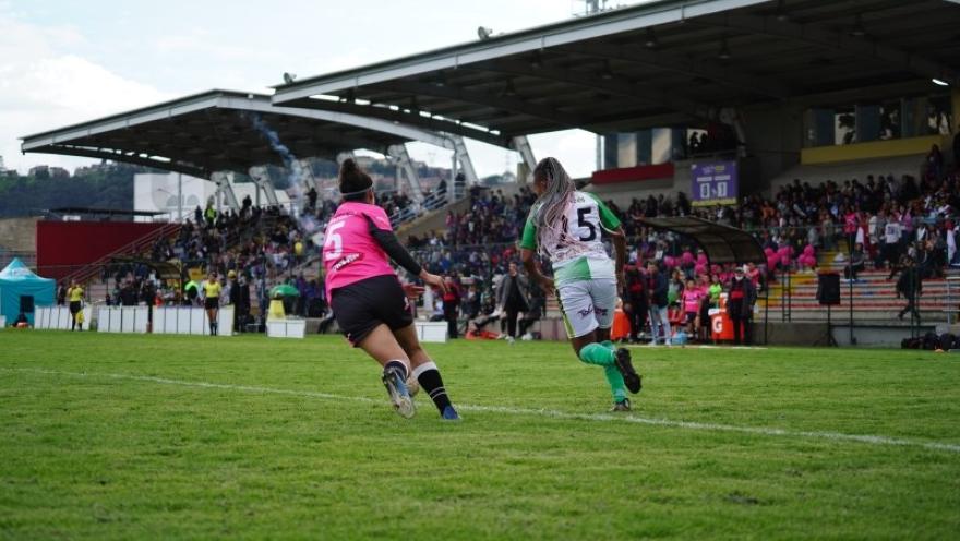 Dos futbolistas disputan una jugada en la cancha del Estadio Olaya Herrera, con las graderías llenas de espectadores durante un partido.
