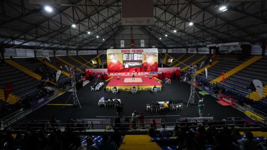 Vista general del Palacio de los Deportes de Bogotá durante una competencia internacional de levantamiento de pesas, con plataforma central, graderías y público asistente.