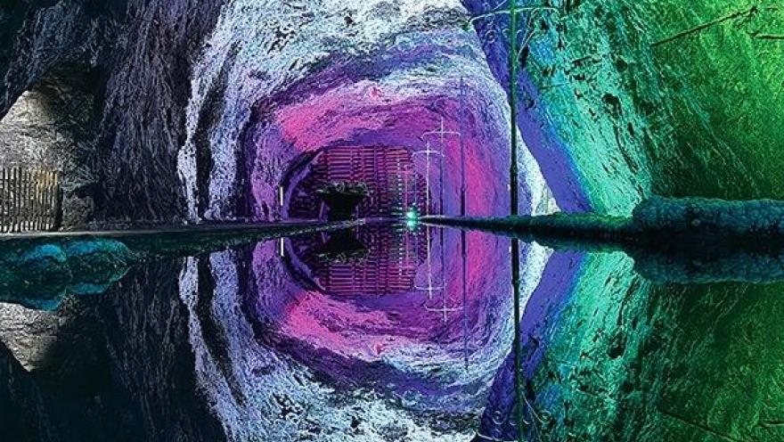 Interior de una mina de sal iluminada con luces verdes, azules y moradas, cuyo reflejo en el agua crea un efecto visual simétrico.