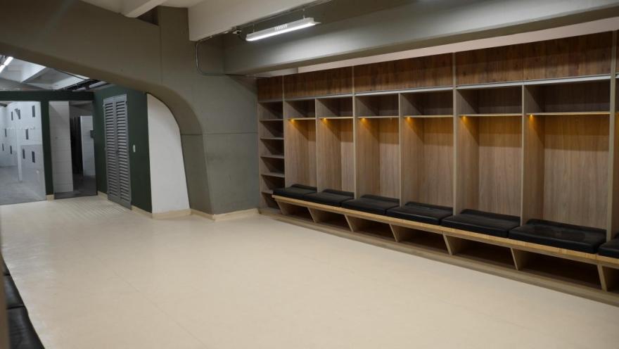 Vestuario del Estadio de Techo con casilleros de madera, bancas acolchadas y acceso a las duchas, en un espacio amplio e iluminado.