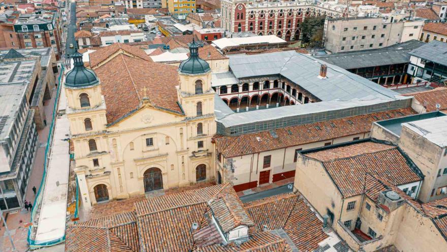 Vista aérea de la Iglesia de Nuestra Señora de La Candelaria, rodeada por los tejados de teja de barro y la arquitectura colonial del centro histórico de Bogotá. Su fachada de estilo colonial destaca entre las calles tradicionales del emblemático barrio La Candelaria.
