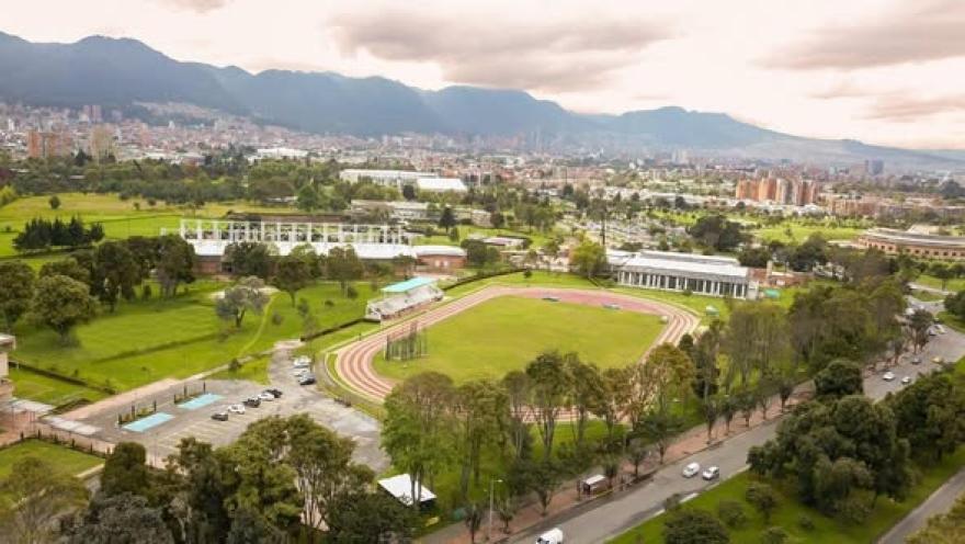Vista aérea del Centro de Alto Rendimiento de Bogotá, con pista de atletismo, zonas deportivas y amplias áreas verdes, rodeadas por la ciudad y los Cerros Orientales al fondo.