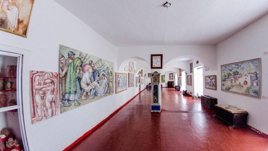Sala de museo con piso de baldosas rojas y paredes blancas, donde se exhiben pinturas y obras de arte a lo largo de un amplio corredor con arcos.