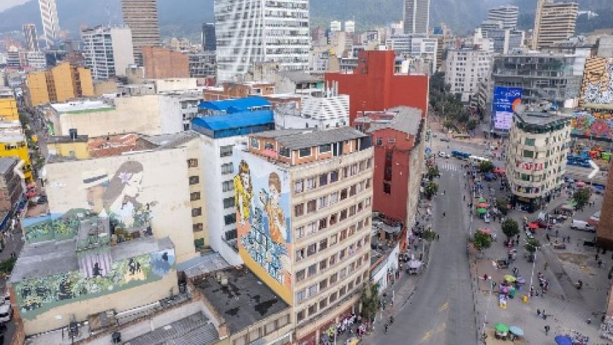 Vista panorámica del sector de San Victorino y el centro de Bogotá, con edificios comerciales, coloridos murales y una concurrida avenida. Al fondo se elevan los Cerros Orientales, enmarcando uno de los principales corredores comerciales y urbanos de la capital.