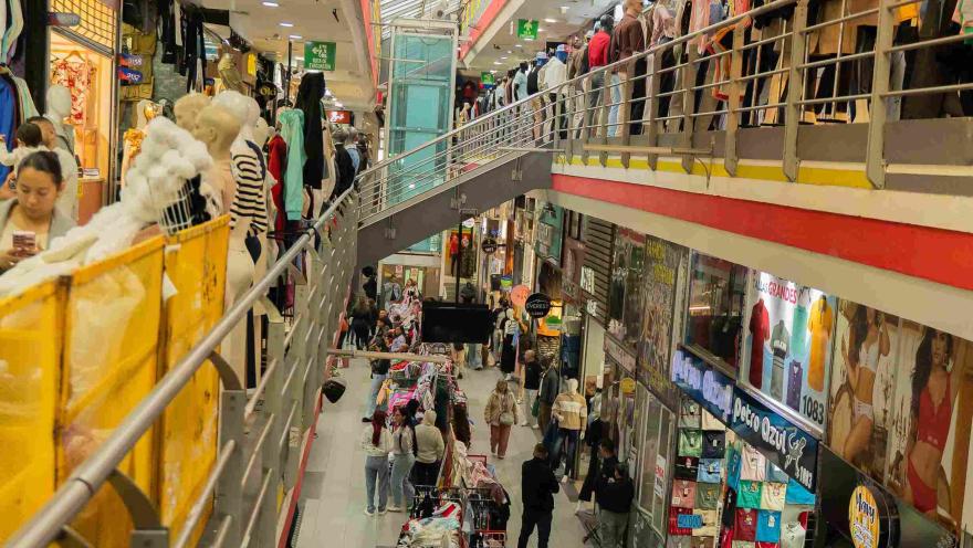 Interior de un concurrido centro comercial en San Victorino, con locales de ropa y accesorios distribuidos en varios niveles. Los pasillos llenos de compradores y vitrinas exhiben la amplia oferta comercial que caracteriza a este emblemático sector del centro de Bogotá.