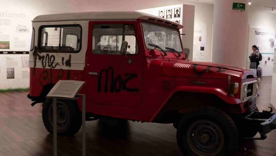 Vehículo Toyota Land Cruiser de color rojo con grafitis, exhibido como pieza histórica en un espacio museográfico.