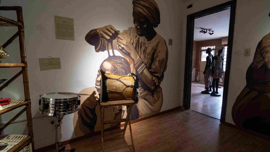 Sala de exposición con un mural de una mujer afrodescendiente tocando un tambor, acompañado de instrumentos musicales tradicionales que resaltan el legado cultural y musical afrocolombiano.