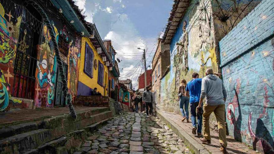 Callejón del Embudo en La Candelaria, con visitantes recorriendo su calle empedrada, rodeada de casas coloridas y muros decorados con arte urbano.