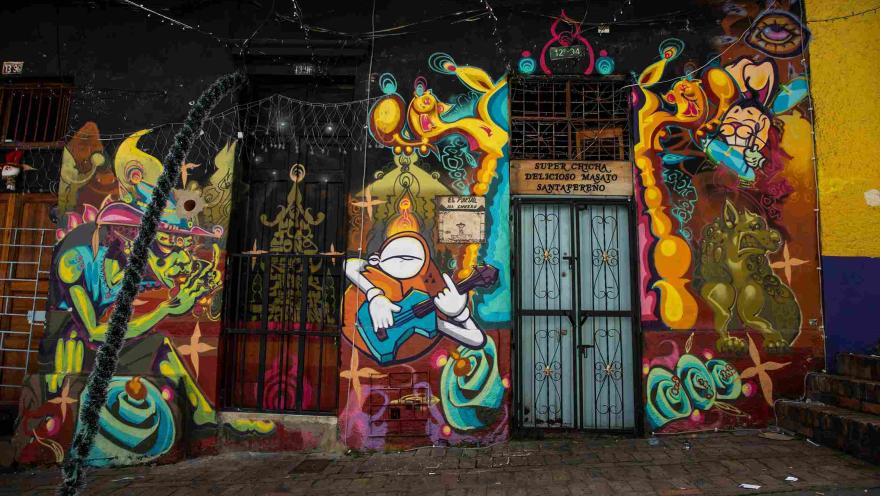 Fachada colorida del Callejón del Embudo, decorada con llamativos murales de arte urbano, figuras fantásticas y referencias a la cultura bogotana.