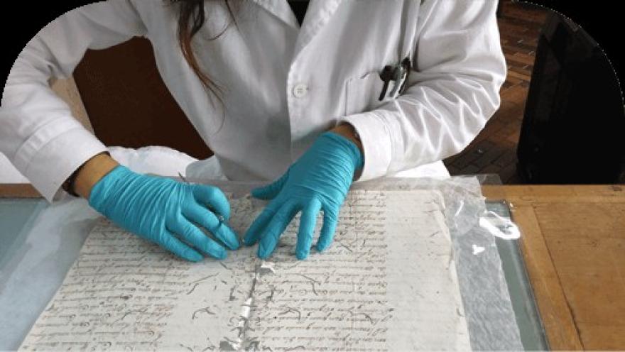 Especialista en conservación documental revisando cuidadosamente un manuscrito histórico con guantes.