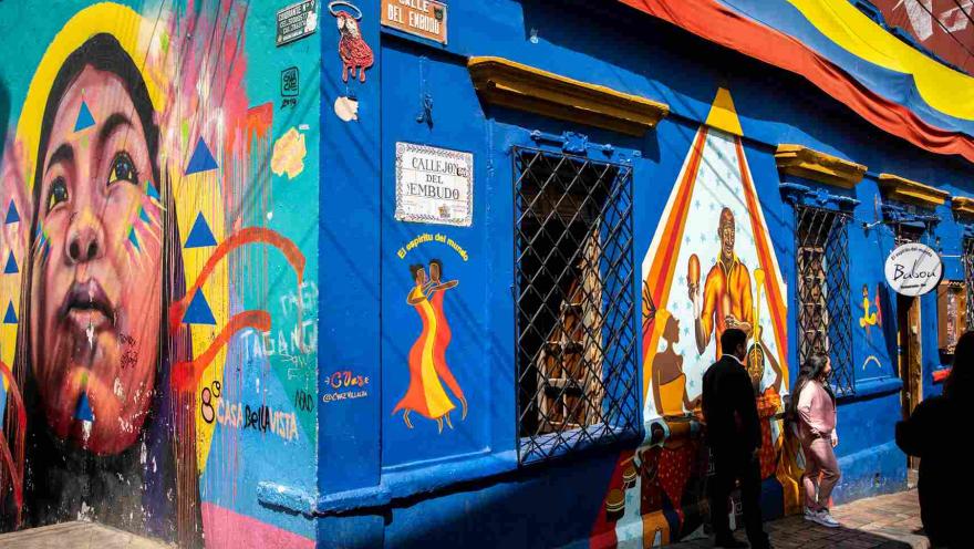 Fachada del Callejón del Embudo, con murales coloridos, arte urbano y visitantes que recorren este emblemático rincón de La Candelaria.