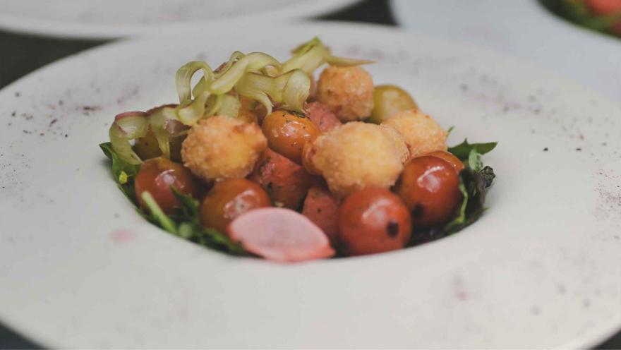 Plato hondo de cerámica blanca con una ensalada gourmet compuesta de tomates cherry, esferas apanadas y vegetales.