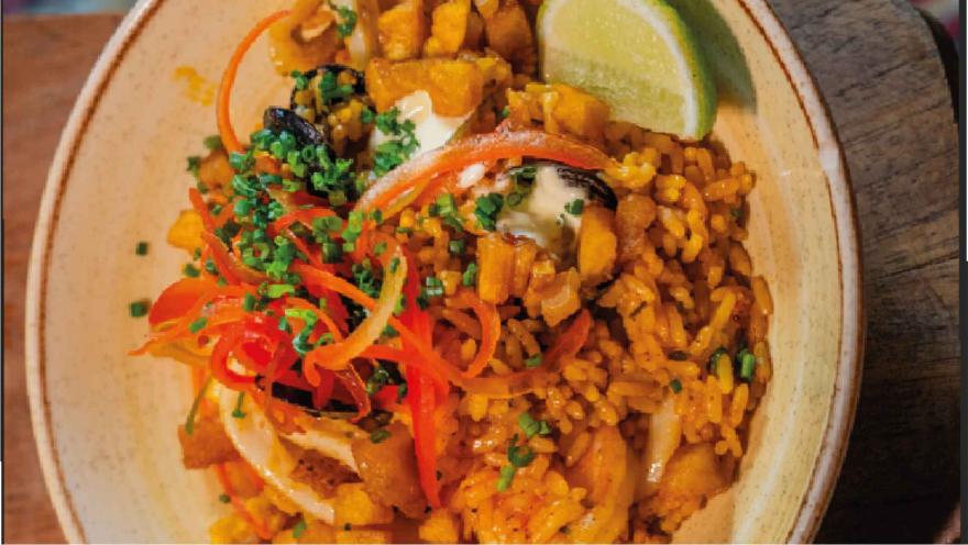 Tazón de arroz preparado con mariscos, cebolla en tiras, verduras picadas y una rodaja de limón al borde.