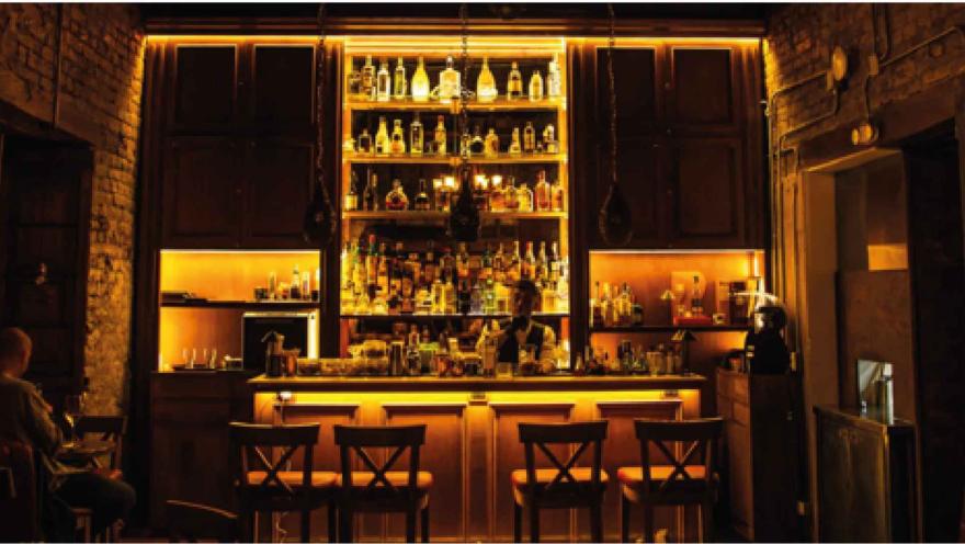  Elegante barra de bar con iluminación cálida amarilla, estantes llenos de botellas de licor y sillas de madera.