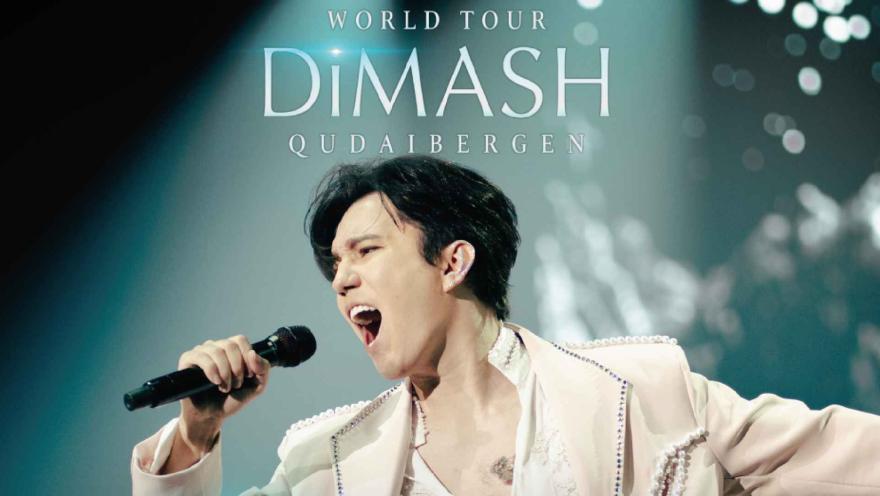 Dimash Qudaibergen, con un elegante traje blanco con detalles plateados, cantando apasionadamente con los ojos cerrados.
