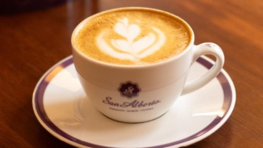 A cup of San Alberto coffee with delicate heart-shaped latte art, served on an elegant saucer on a wooden table.