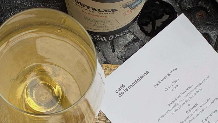 A glass of white wine next to the menu at Café de la Madeleine, on a table that invites you to discover its gastronomic concept.