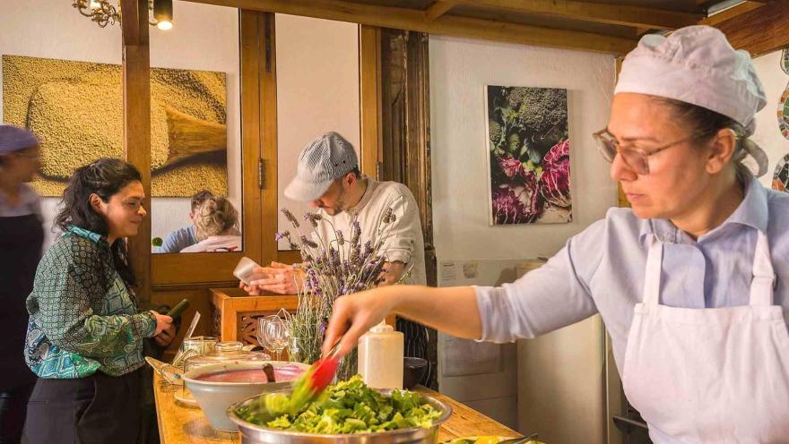 Cocineros preparan alimentos frescos en un ambiente cálido y artesanal, con ingredientes vegetales dispuestos para su elaboración.