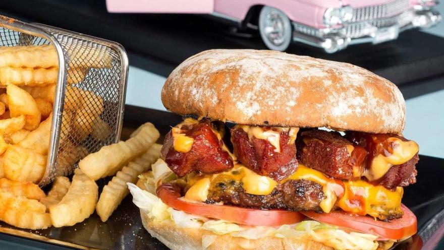  Hamburguesa doble con queso, tocino y salsas, acompañada de papas, en una presentación inspirada en los clásicos años 50.