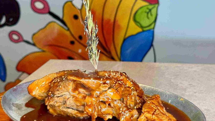 A plate of meat drenched in sauce and garnished with sesame seeds.