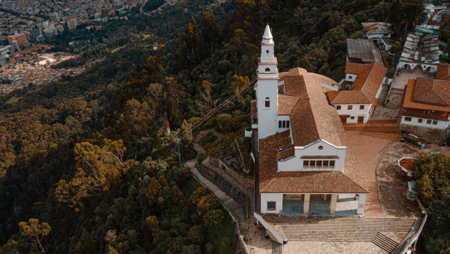 Vista aérea de la iglesia de Monserrate, rodeada por el bosque y con Bogotá extendiéndose al fondo.