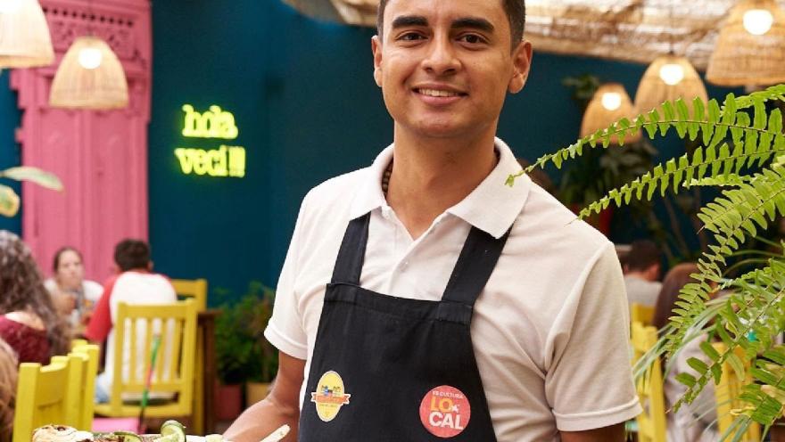 Mesero sonriente presenta un plato de comida, en el colorido y acogedor ambiente interior del restaurante.