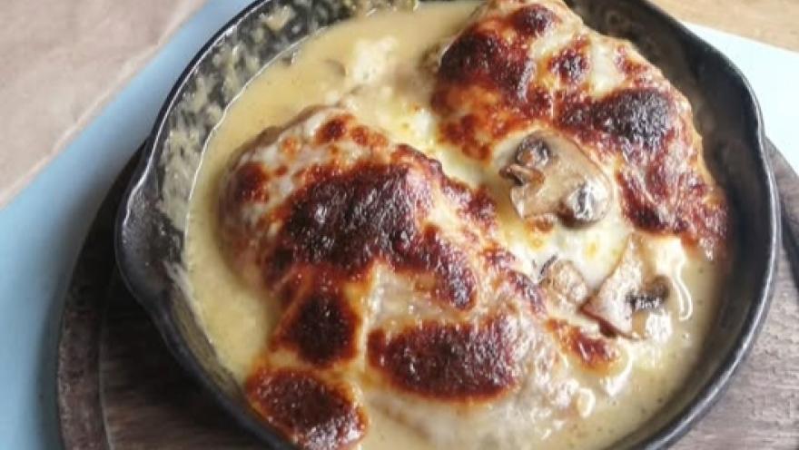 Plato de pollo gratinado con champiñones, servido en una sartén de hierro.