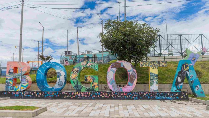 Espacio público de Ciudad Bolívar con coloridas letras decoradas con arte urbano, junto a una cancha deportiva y murales.