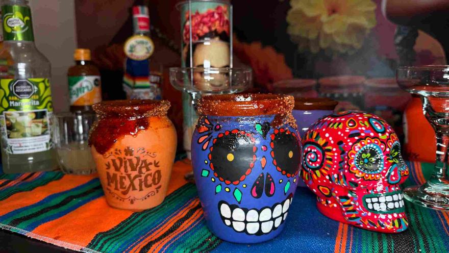 Clay cups decorated with Mexican motifs and traditional drinks, alongside colorful skulls.