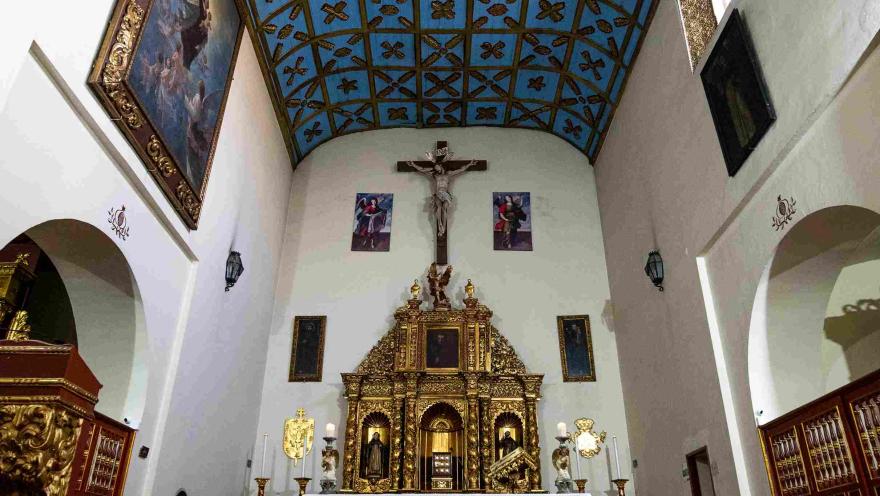 Altar lateral de la Iglesia de San Juan de Dios, con un elaborado retablo dorado, imágenes religiosas y un techo de madera decorado en tonos azules.