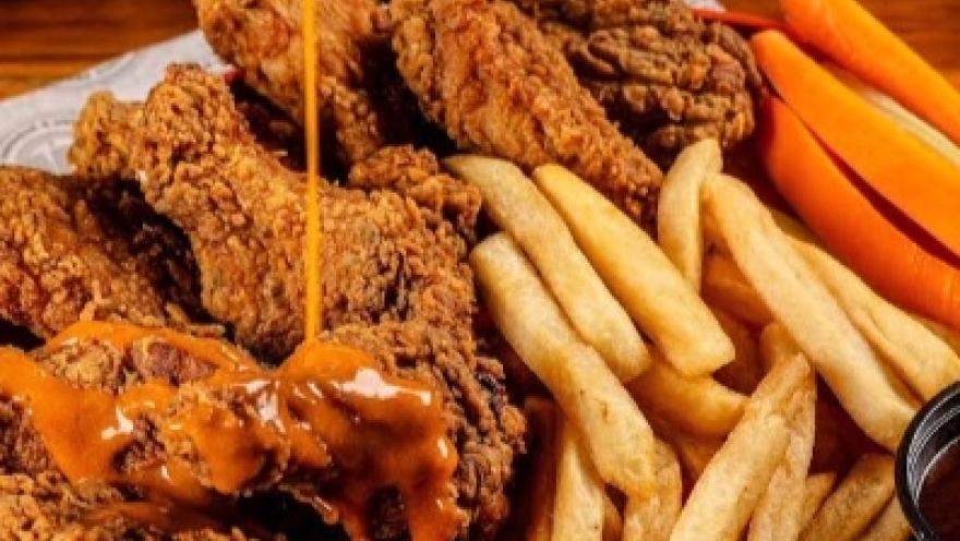 Alitas de pollo crujientes con salsa, acompañadas de papas fritas y bastones de zanahoria, servidas en una bandeja.