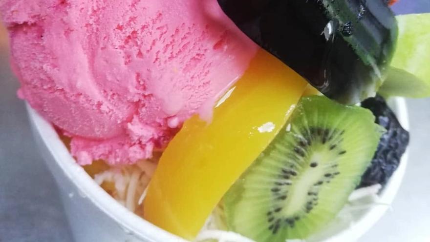 Ensalada de frutas con helado de fresa, mango, kiwi y chocolate, acompañada de coco rallado.