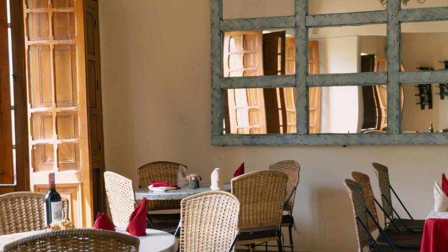 Restaurant dining room with warm decor, tables set for diners, wicker chairs, wooden doors, and large mirrors that expand the space.