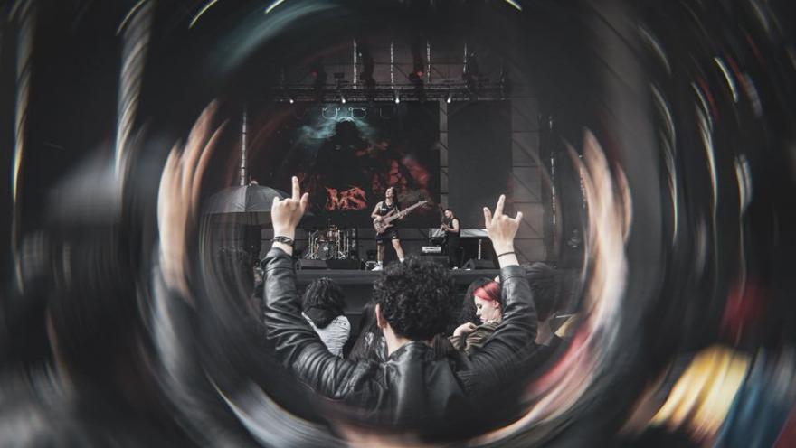 Público en concierto de rock levantando las manos frente al escenario, visto a través de un efecto circular que resalta la energía del momento.