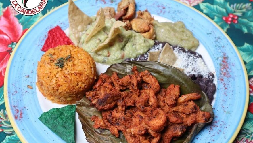 A Mexican food dish with seasoned chicken, rice, guacamole, beans, totopos, and salsas, served on a banana leaf.