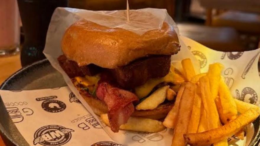 Hamburguesa con carne, queso y tocino, acompañada de papas fritas, servida en un plato de restaurante.